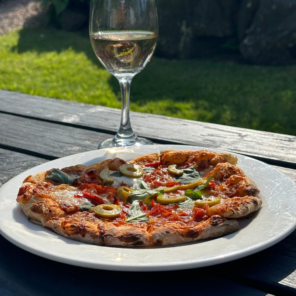 A vegetarian pizza with a glass of white wine, on a Beer Garden table in the sunshine.